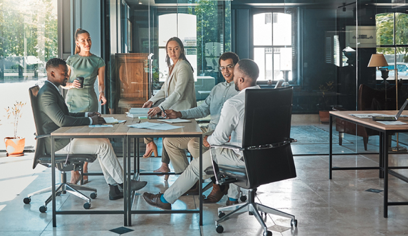 three men sitting around table, two women standing at table